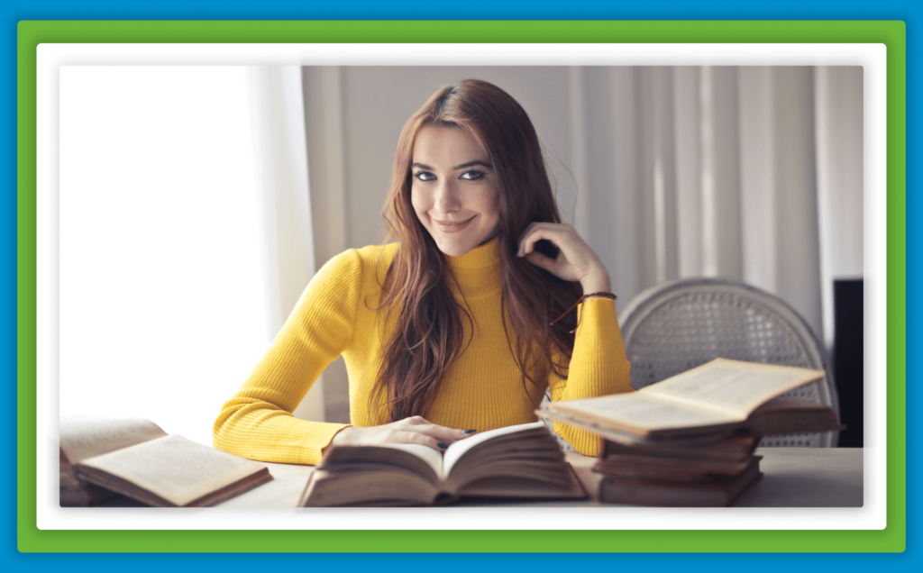 A smiling woman with books on a table.