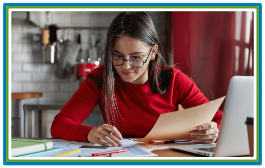 A young woman with glasses reviews documents at a desk.