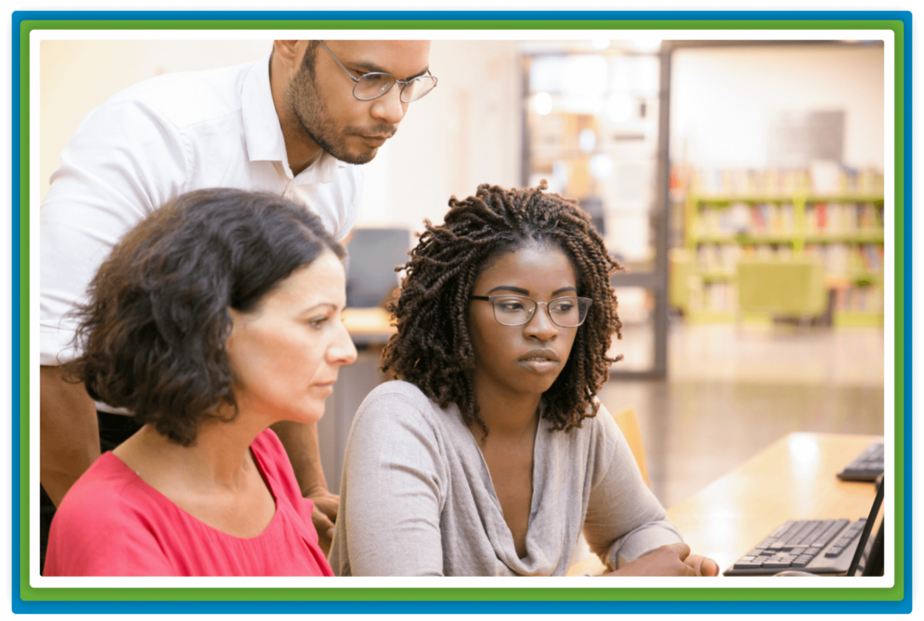 Three people focused on a computer screen in a library.
