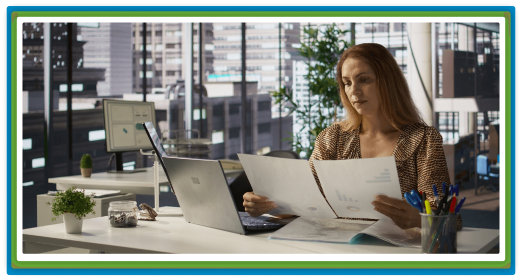 A woman works at a desk, reviewing documents.